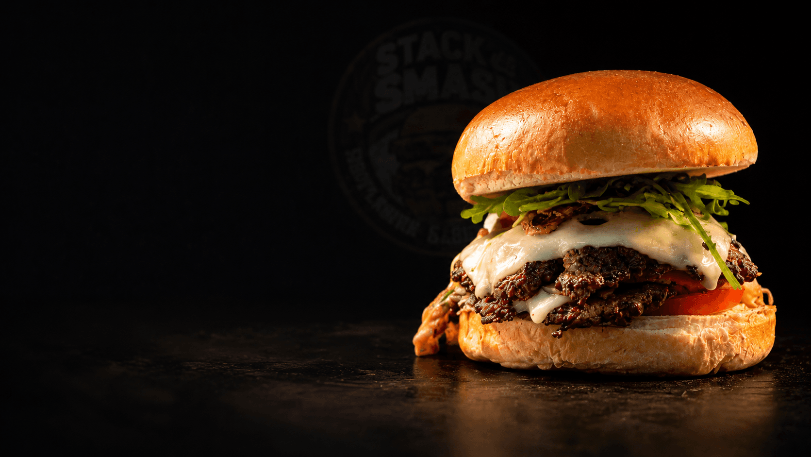Gourmet smash burger with arugula and melted cheese on a dark slate surface