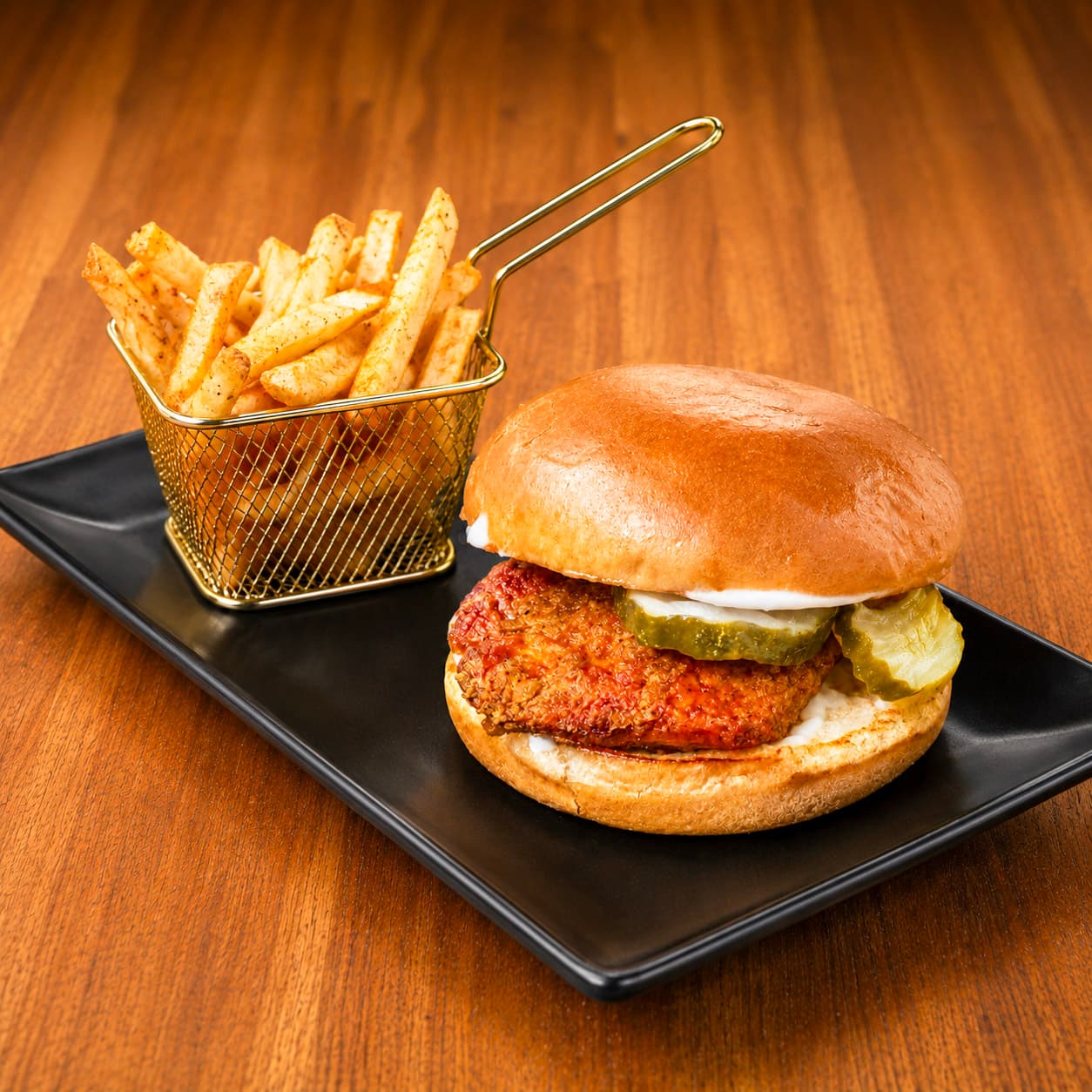 Fried chicken sandwich with pickles and french fries on a black plate